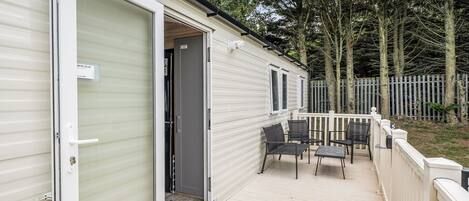 A mobile home with a deck, outdoor seating, and a fenced yard.