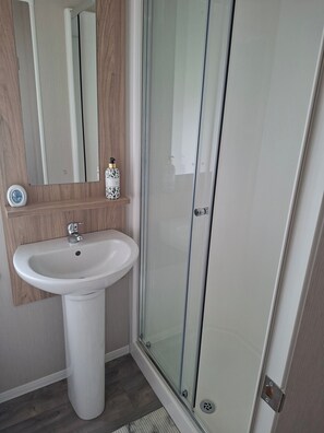 A bathroom with a white pedestal sink, a mirror, and a glass shower enclosure.