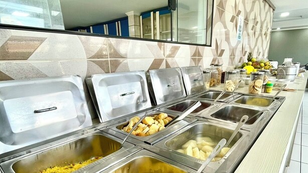 A buffet with various food items in metal containers, a tiled backsplash, and a counter with a fruit display.