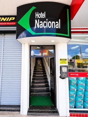 A hotel entrance with a staircase leading to the lobby, a sign for Hotel Nacional, and a visible store with products. - Hotel Nacional (ARAPIRACA)