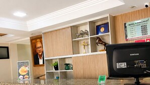 A hotel reception desk with a Samsung monitor, a framed portrait, and a sign listing room rates.