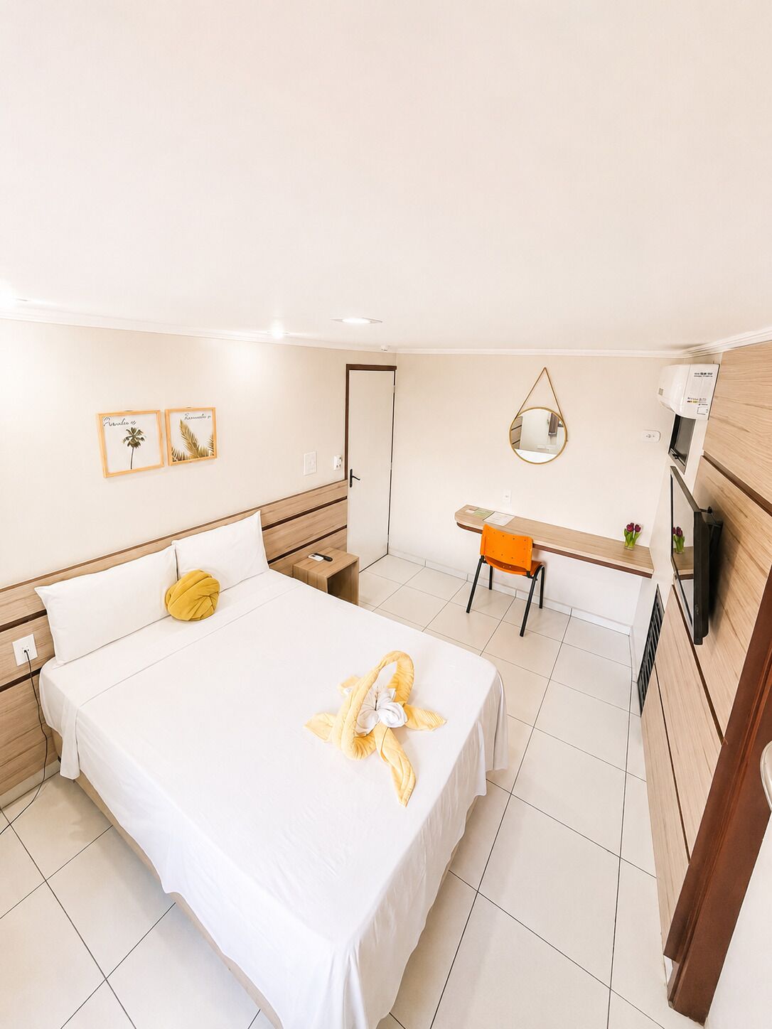 A hotel room with a bed, a desk, a chair, a mirror, and a TV.