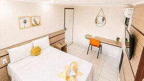 A hotel room with a bed, a desk, a chair, a mirror, and a TV.