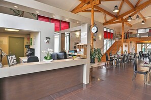 Zona de recepción de hotel con escritorio, sillas, un reloj y una escalera que lleva a pisos superiores.