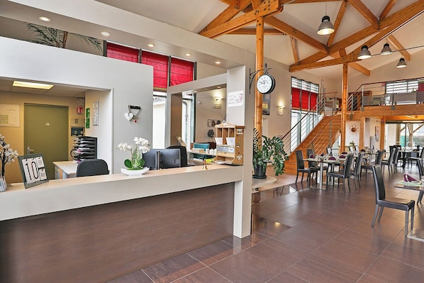 A hotel reception area with a desk, chairs, a clock, and a staircase leading to upper floors. - Zenao Appart'hôtels Sainte-Soulle (Sainte-Soulle)