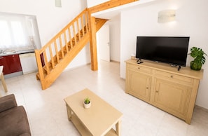 A living room with a wooden staircase, a television on a cabinet, a small table with a plant, and a kitchen area with a red cabinet and white appliances. - Zenao Appart'hôtels Sainte-Soulle (Sainte-Soulle)