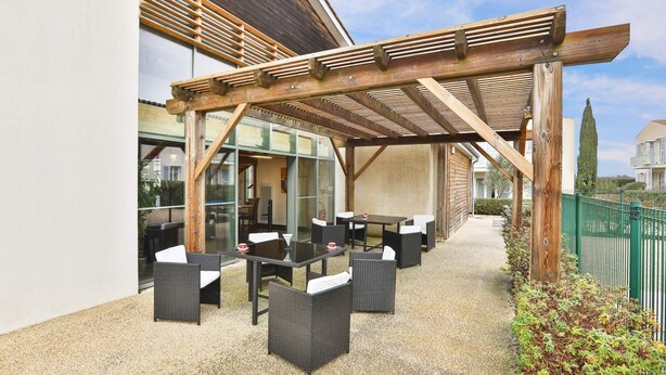 An outdoor patio with wicker furniture and a wooden pergola. - Zenao Appart'hôtels Sainte-Soulle (Sainte-Soulle)
