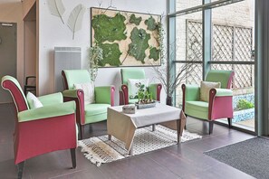 Ein modernes Wohnzimmer mit grün und rot gepolsterten Sesseln, einem beigen Couchtisch und einem großen Fenster mit Blick auf einen Garten.