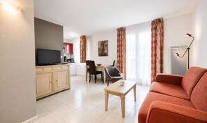 Una sala de estar con sofá, televisor, mesa de comedor con sillas y una zona de cocina con armarios y estufa.
