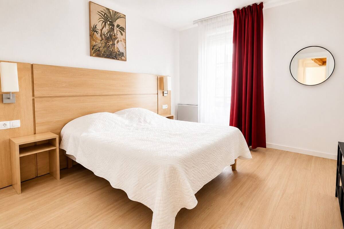 Un dormitorio ordenado con cama, mesitas de noche, un espejo y una obra de arte colgada en la pared.