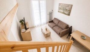 A modern living room with a sofa, a coffee table, a desk with a computer, and a painting on the wall. - Zenao Appart'hôtels Sainte-Soulle (Sainte-Soulle)