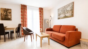 Ein Wohnzimmer mit einer Couch, einem Esstisch mit Stühlen, einer Lampe und Kunstwerken an den Wänden.
