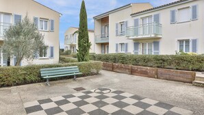 A courtyard with a checkered floor, a wooden bench, and a tall tree. - Zenao Appart'hôtels Sainte-Soulle (Sainte-Soulle)