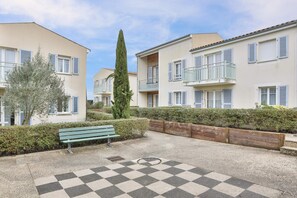 A courtyard with a checkered floor, a wooden bench, and a tall tree. - Zenao Appart'hôtels Sainte-Soulle (Sainte-Soulle)