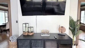 En stue med et stort fladskærms-tv monteret på væggen, et mørkt træskab nedenunder og en potteplante til højre.
