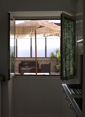 A kitchen with a window overlooking a patio area with a thatched umbrella and outdoor furniture. - Naples Holiday House with Private Terrace, near Station, Metro, Airport (Napoli)