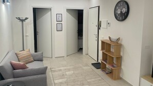 Una sala de estar moderna con un sofá gris, una estantería de madera, un reloj y una puerta que da a otra habitación.