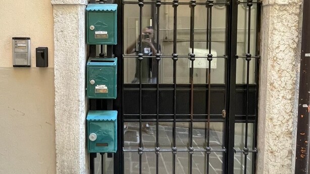 Una reja de metal negro con un arco de piedra, un buzón verde y un escalón que lleva a la puerta.