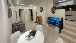 Una sala de estar moderna con televisor de pantalla plana, una mesa de comedor con sillas, un sofá, un perchero y una escalera que lleva a un nivel superior.
