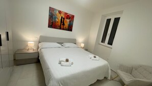 Un dormitorio con cama, lámparas de noche, una silla y un cuadro en la pared.
