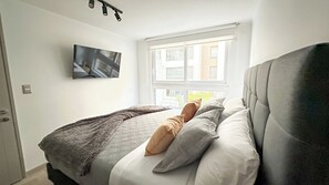 A bedroom with a bed, a TV mounted on the wall, and a window with a view of buildings. - Modern, centrally located apartment steps from the Movistar Arena (Santiago)