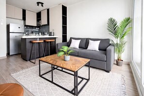 Ein modernes Wohnzimmer mit Küche, grauem Sofa, Couchtisch und Topfpflanzen.