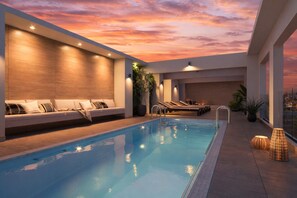A pool area with a sunset view, a seating area with cushions, and lounge chairs. - Modern, centrally located apartment steps from the Movistar Arena (Santiago)