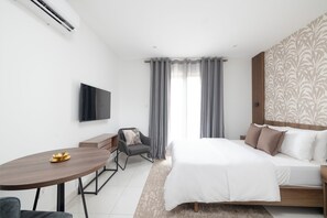 A modern hotel room with a bed, a desk, and a TV. - Suite with Balcony at The Bantree (Accra)