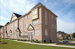 A multi-story brick apartment building with a symmetrical facade, large windows, and a central entrance. - Sleek 3 bedroom contemporary stay - close to 401, Ajax Go Station and Downtown (Ajax)