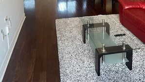 En moderne stue med en rød sofa, et glasbord og et køkken i baggrunden.