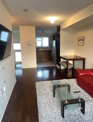 A modern living room with a red sofa, a glass coffee table, and a kitchen in the background. - Sleek 3 bedroom contemporary stay - close to 401, Ajax Go Station and Downtown (Ajax)