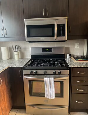 A kitchen with stainless steel appliances, including a microwave and an oven, with wooden cabinets and a granite countertop. - Sleek 3 bedroom contemporary stay - close to 401, Ajax Go Station and Downtown (Ajax)