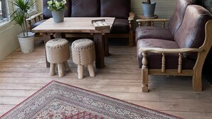 A sunroom with a wooden table, two leather sofas, a small round table, and potted plants. - Quiet vacation home "Zum Holzwurm" with large terrace & winter garden! (Molbergen)