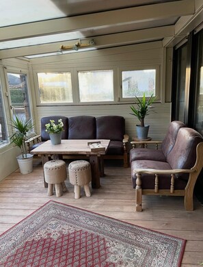 A sunroom with a wooden table, two leather sofas, a small round table, and potted plants.