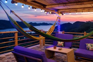 Un hamac, des chaises violettes, une table et une vue sur l’eau et les montagnes.