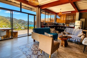 Un vaste espace de vie doté d’une grande fenêtre offrant une vue sur la mer et les montagnes, d’un coin bar et d’un espace détente agrémenté d’un tapis à motifs.