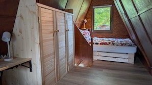 Ein Schlafzimmer im Loft-Stil mit einem Holzschrank, einem Schreibtisch, einem Bett mit bunter Bettdecke und einem Fenster mit Blick auf Grünflächen.