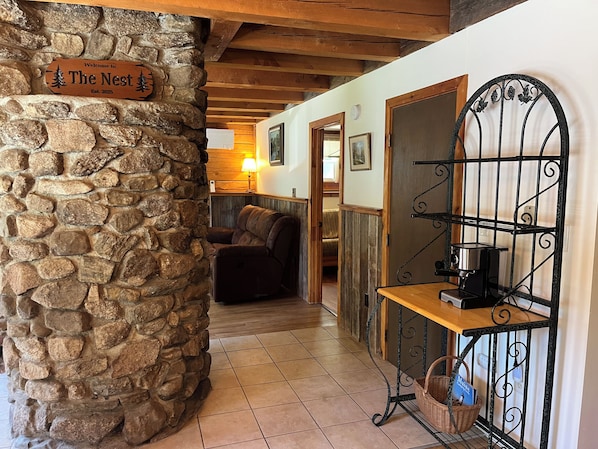 A stone wall with a welcome sign, a wooden bench with a basket, and a cozy seating area with a lamp.