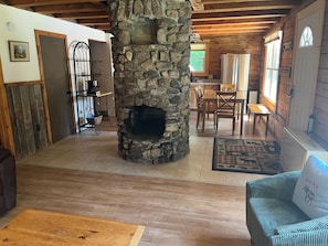 A cozy cabin interior with a stone fireplace, wooden furniture, and a dining area.