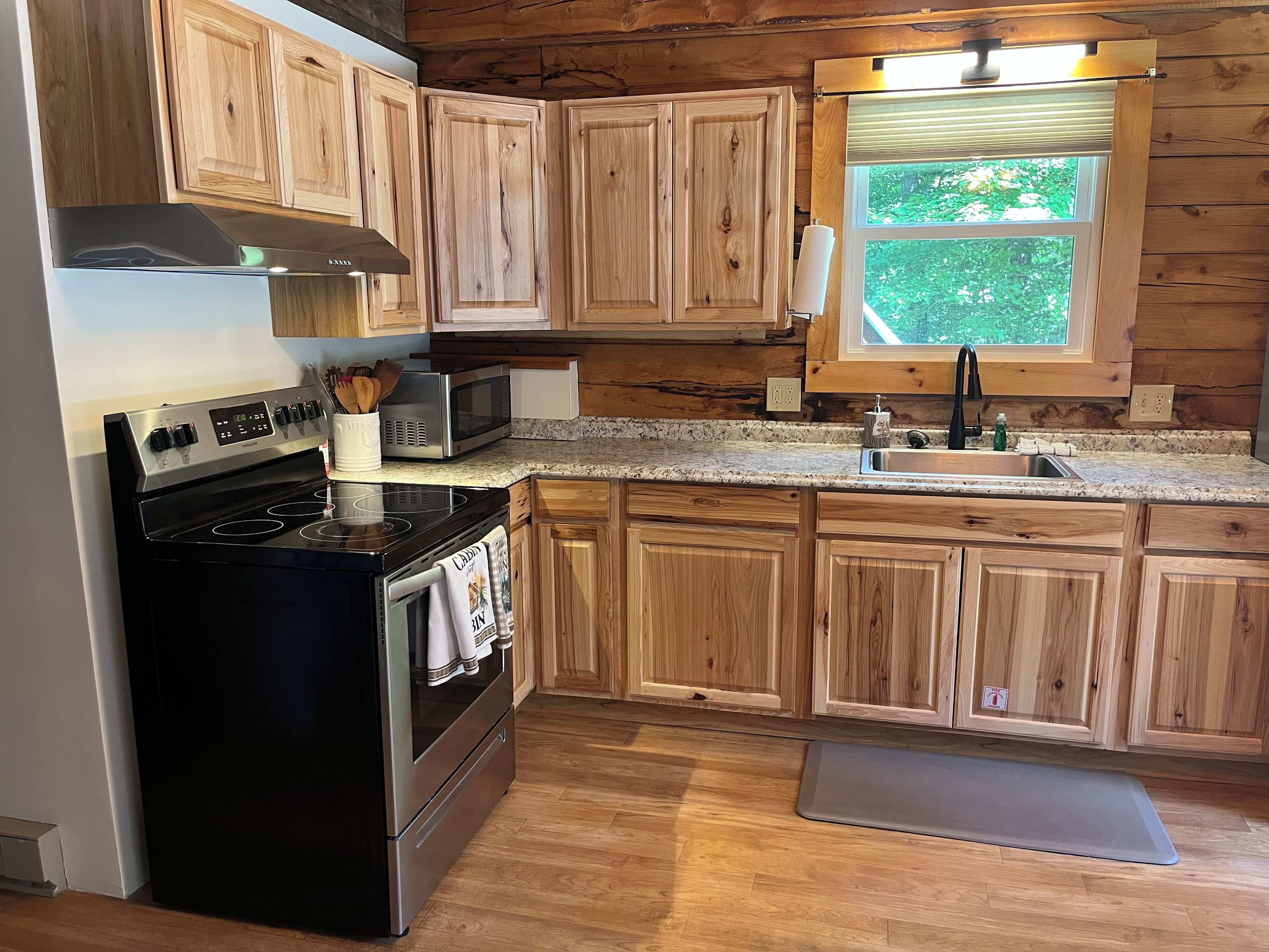 A kitchen with wooden cabinets, a stainless steel stove, a microwave, and a window with a view of greenery.