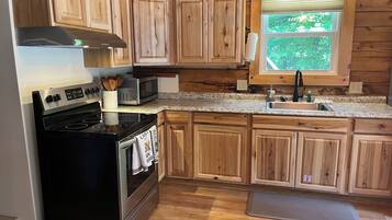 A kitchen with wooden cabinets, a stainless steel stove, a microwave, and a window with a view of greenery.