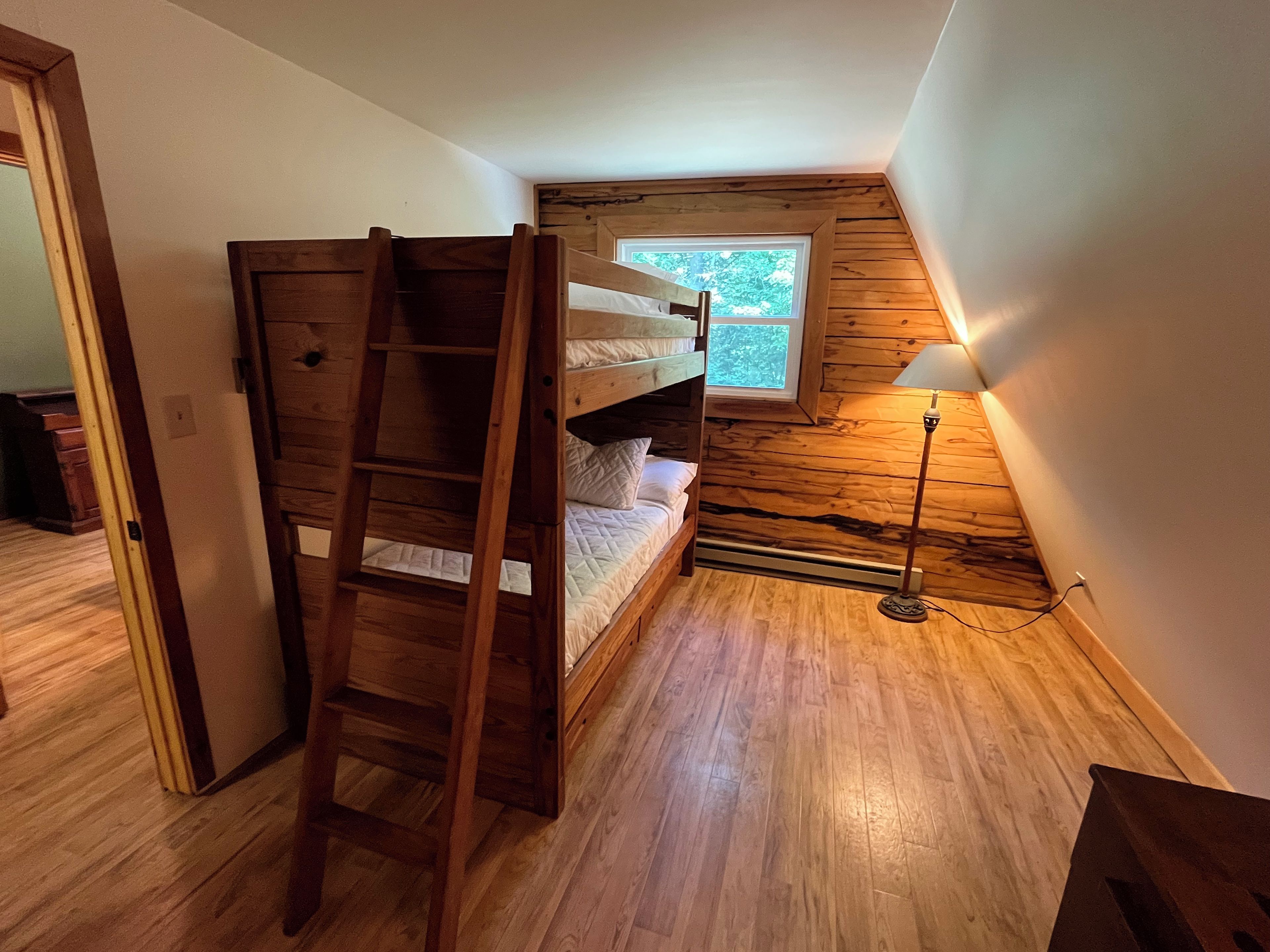 A room with a bunk bed, a ladder, a window, and a floor lamp.
