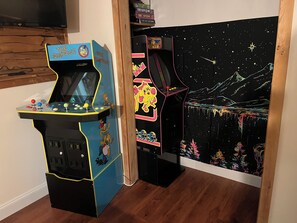 Two arcade machines with 'The Simpsons' branding, one with a space-themed backdrop, and a television mounted on the wall.