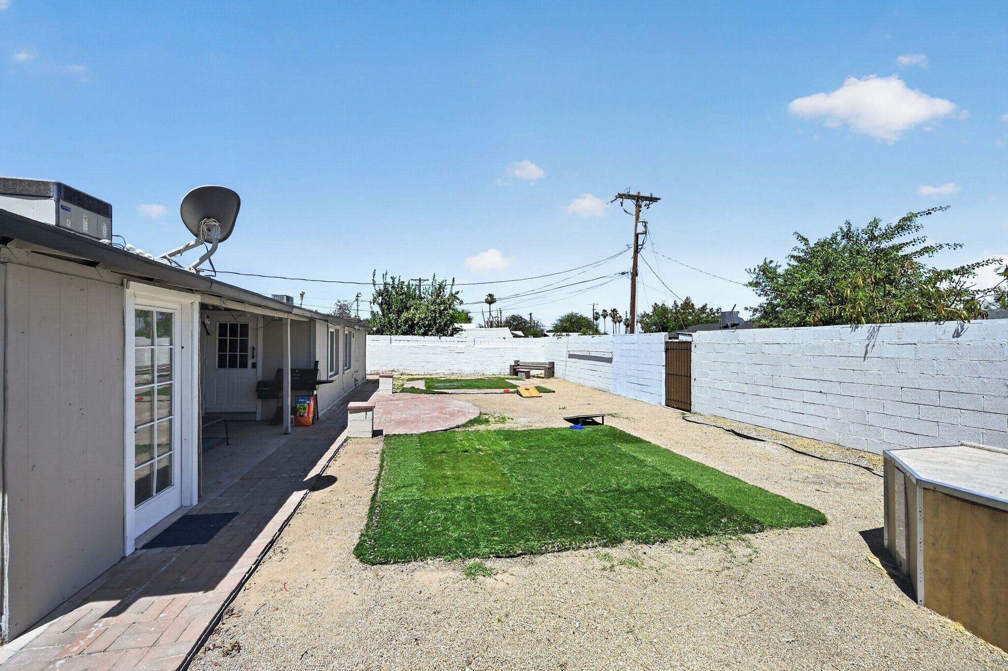 Un jardin avec une pelouse, une terrasse et un mur en briques blanches.