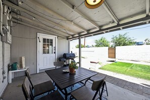 Une terrasse couverte avec une table et des chaises, un barbecue et une porte donnant sur un jardin.