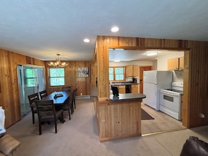 A wooden interior with a dining table, chairs, a kitchen with a refrigerator and stove, and a chandelier. - RIVER SIDE walking distance to town/the lake & Rocky Mnt Natl Park! 3-bedroom (Grand Lake)