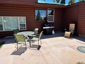 Eine Terrasse mit rundem Tisch, Stühlen, einem Grill und einem Sessel.