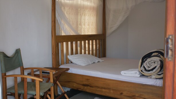 Uma cama de solteiro com estrutura de madeira, uma cadeira verde e um edredom branco.