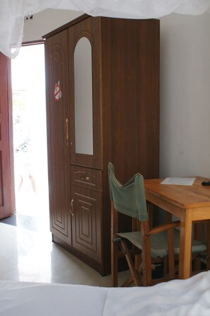 A room with a wooden wardrobe, a wooden table, and a green chair. - Makeseni Lodge (Arusha)