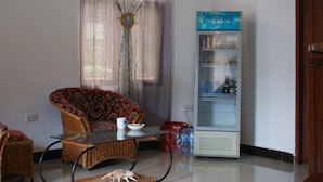 Uma sala de estar com um sofá de vime, uma mesa de centro de vidro e uma geladeira.